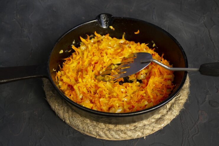 Sautéing onions and carrots in a skillet to create a flavorful base. Chopped onions and grated carrots being sautéed in a black skillet.