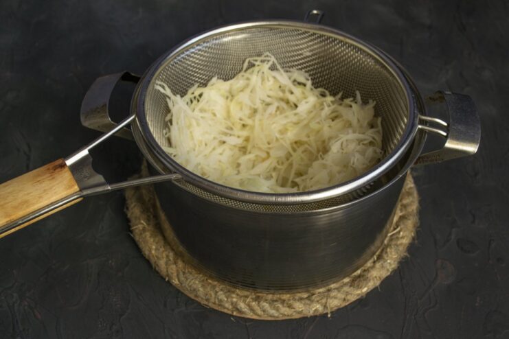 Boiling sauerkraut to soften it and reduce its sourness before adding to the filling. Sauerkraut boiling in a pot of water on the stove.