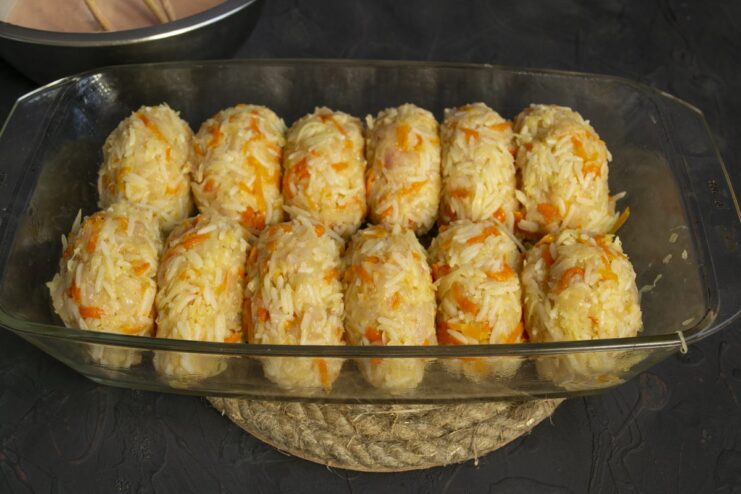 Shaping the lazy cabbage rolls and arranging them in a baking dish before baking. Uncooked oval-shaped lazy cabbage rolls arranged in a white ceramic baking dish.