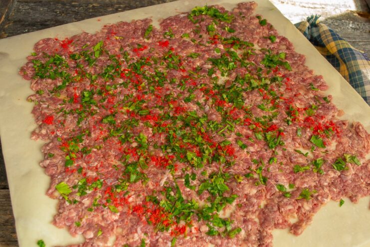 Seasoning the Filling with Parsley and Paprika The meat filling on the dough being sprinkled with chopped fresh parsley and red paprika.