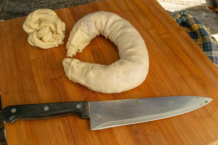 Coiling the Dumpling Roll into a Spiral The long dumpling roll being coiled into a spiral or snail shape on a wooden board.
