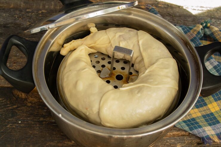 Placing the Pelmeni Coil in the Steamer The spiral-shaped dumpling roll placed on a greased steamer rack inside a pot.
