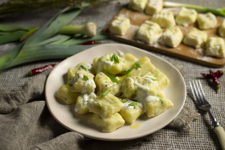 A plate of cooked lazy varenyky with potato, tvorog, and onion, garnished with sour cream and green onions.