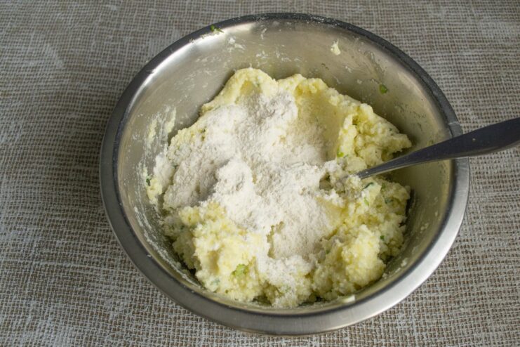 Sprinkling all-purpose flour into the bowl with the potato and tvorog mixture.