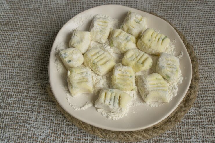 Uncooked lazy varenyky pieces coated in flour on a wooden board.
