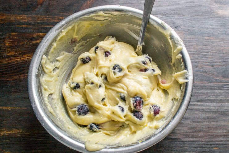 Step 6: Gently folding blueberries into the batter to avoid crushing them A spatula gently folding blueberries into the muffin batter in a bowl.