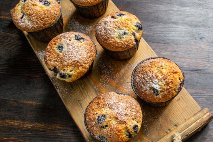 Finishing touch: Dusting warm muffins with powdered sugar Freshly baked lemon blueberry muffins being dusted with powdered sugar using a sieve.