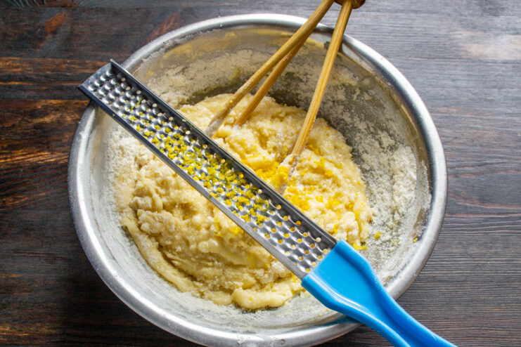 Adding fresh lemon zest for a bright citrus flavor Grating fresh lemon zest directly into the muffin batter in a bowl.