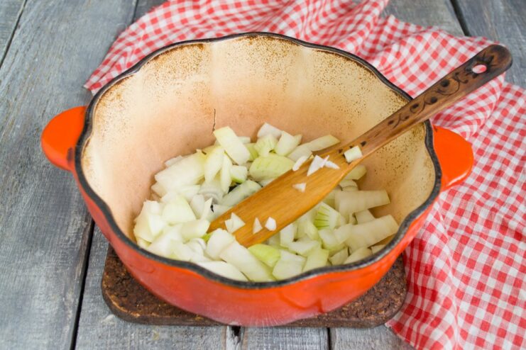Sautéing aromatics to build the stew's flavor base Chopped onion and minced garlic being sautéed in a pot until fragrant.