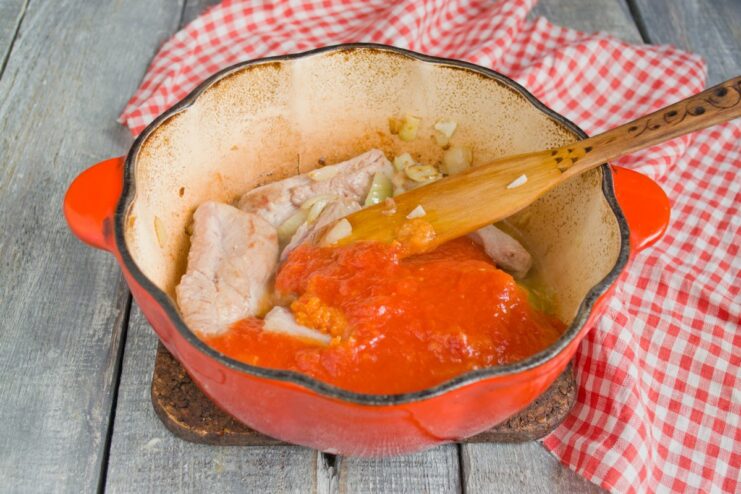 Adding tomato purée for a rich and tangy sauce Tomato purée being added to the seared pork ribs in the pot.