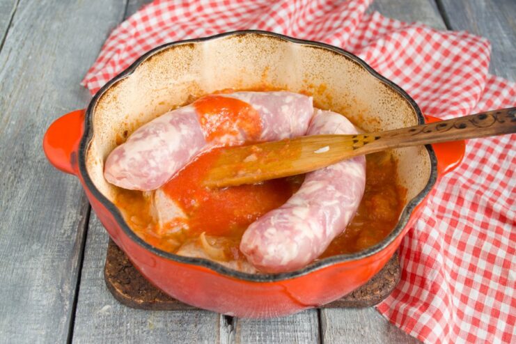 Cooking the sausages whole keeps them juicy and intact Whole raw pork sausages being placed into the pot with ribs and tomato sauce.