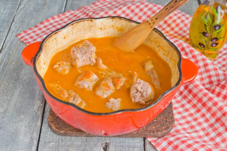 Slow-cooking the pork ribs and sausage for maximum tenderness Pork ribs and whole sausages simmering in a rich tomato-based sauce in a Dutch oven.