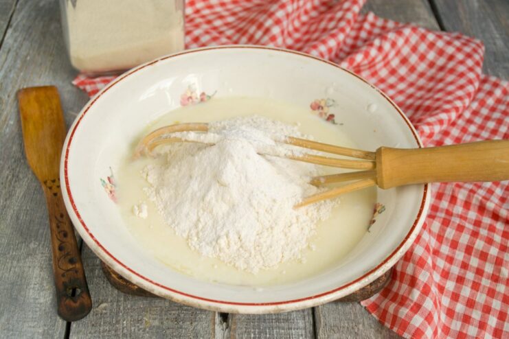 Combining wet and dry ingredients for the pancake batter Dry ingredients like flour and semolina being added to the wet egg and kefir mixture.