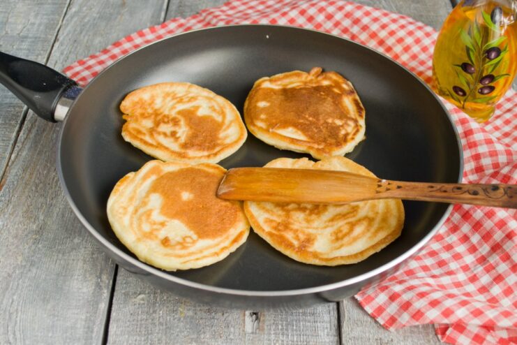 Frying the pancakes until they are golden and fluffy Small, thick pancakes being fried to a golden-brown color in a skillet.