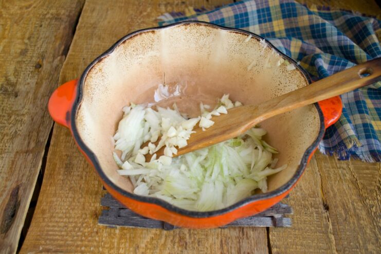 Sautéing onion and garlic to create a fragrant base for the meat sauce. Chopped onion and garlic being sautéed in a pot with vegetable oil.