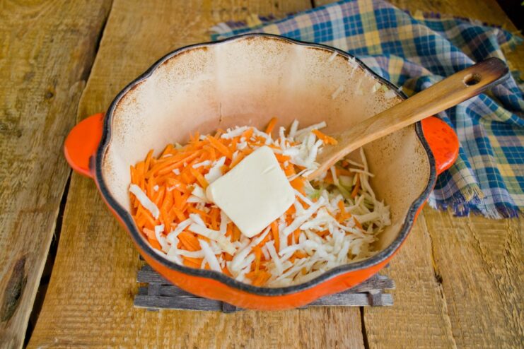 Adding vegetables and butter to soften them and release their juices for a richer sauce. Grated carrots and celery root with a pat of butter being added to the pot with onions.