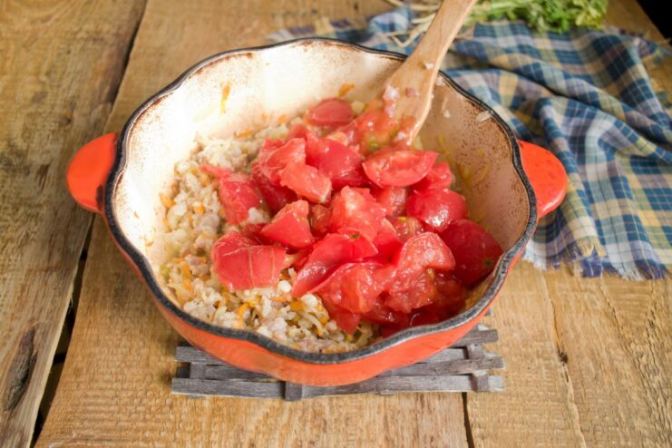 Adding canned tomatoes to create the rich, tangy base of the meat sauce. Canned chopped tomatoes being added to the browned meat and vegetable mixture in the pot.