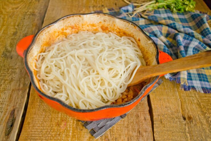 Combining the cooked pasta directly with the sauce ensures every piece is perfectly coated. Cooked pasta being tossed with the finished meat sauce in a large pot.