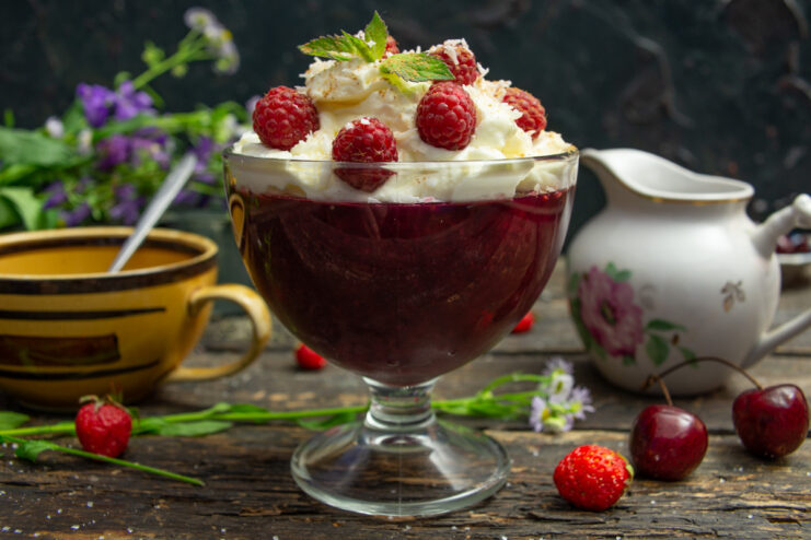 A glass dessert bowl filled with raspberry jelly and topped with whipped cream, fresh raspberries, and mint.