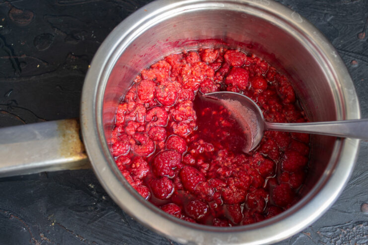 Releasing the juice by mashing raspberries A spoon mashing fresh raspberries in a pot to release their juice.