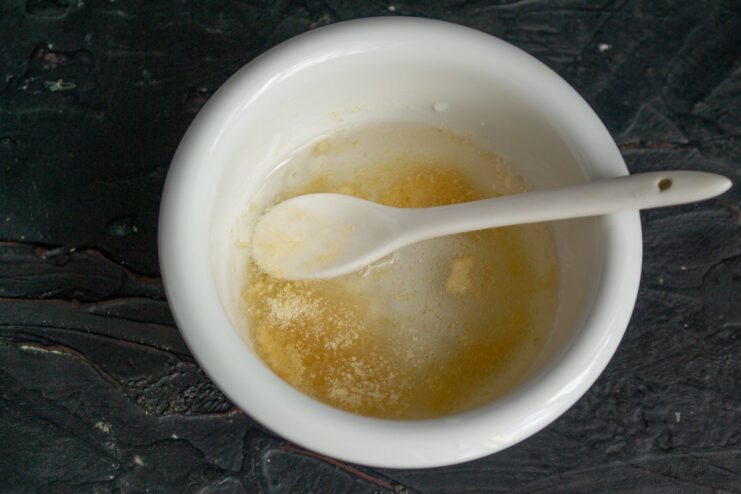 Blooming the gelatin for the jelly A hand pouring powdered gelatin from a packet into a small glass bowl.