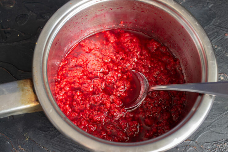 Cooking the raspberries to extract maximum flavor Raspberries cooking and breaking down in a pot on the stove.