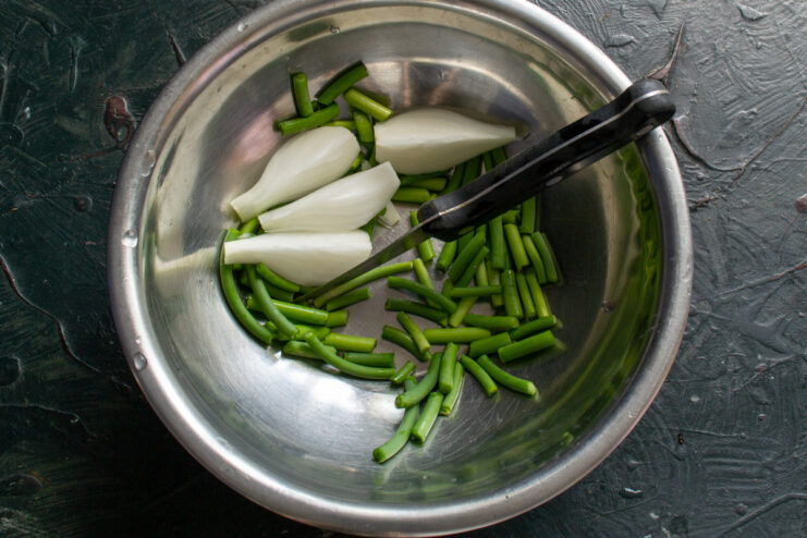 Preparing Garlic Scapes for Pickling Close-up of hands cutting green garlic scapes on a wooden board.