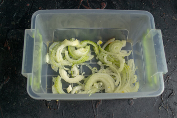Thinly sliced onion half-rings on a cutting board.