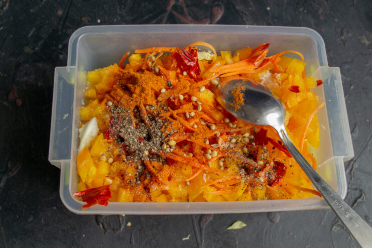 A bowl of mixed vegetables with various spices and seasonings being added on top.