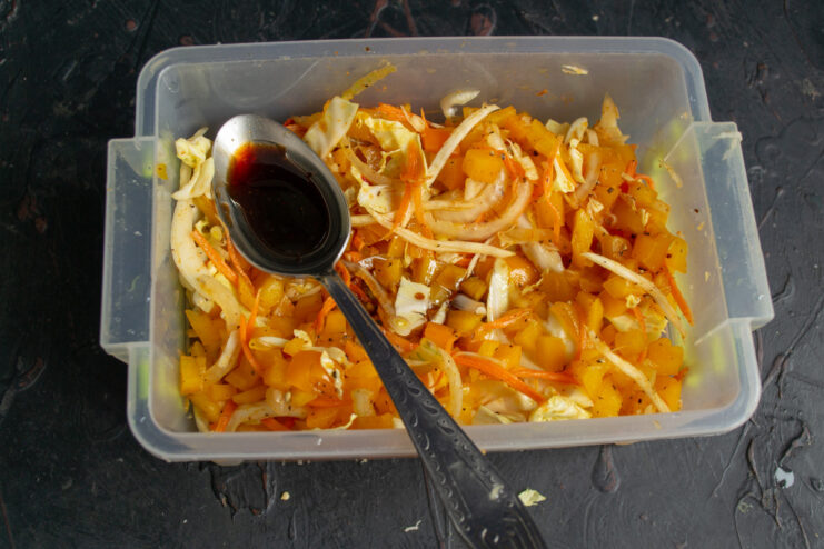 Pouring oil from a bottle into a container with vegetables and spices.