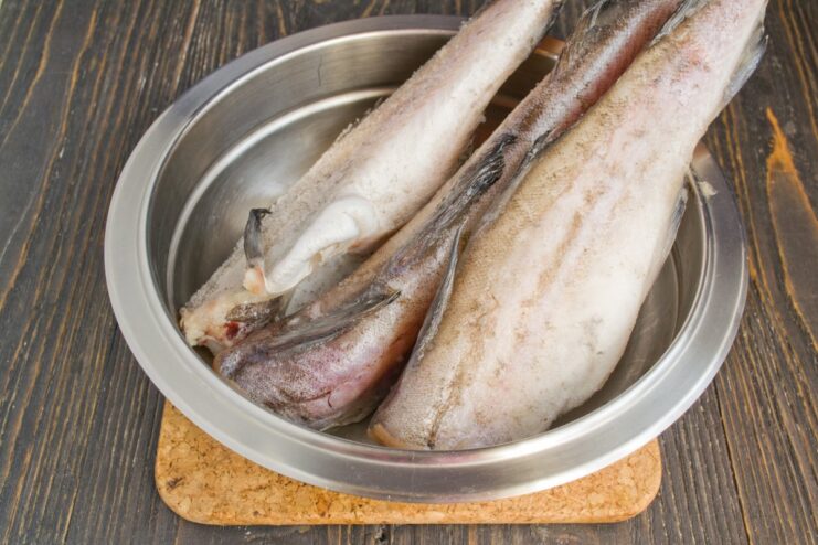 How to Properly Thaw Frozen Pollock for Cooking Two whole frozen pollock fish thawing on a wooden cutting board.
