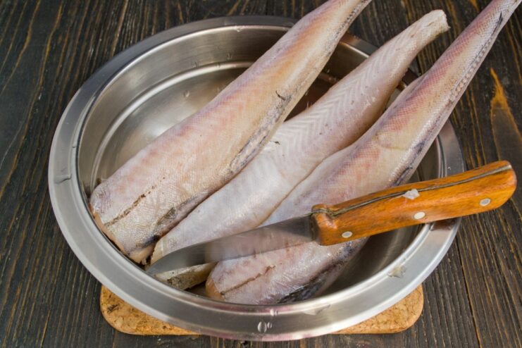 Step-by-Step: Preparing Whole Pollock for Boiling A person's hands cleaning a whole pollock fish under running water in a kitchen sink.