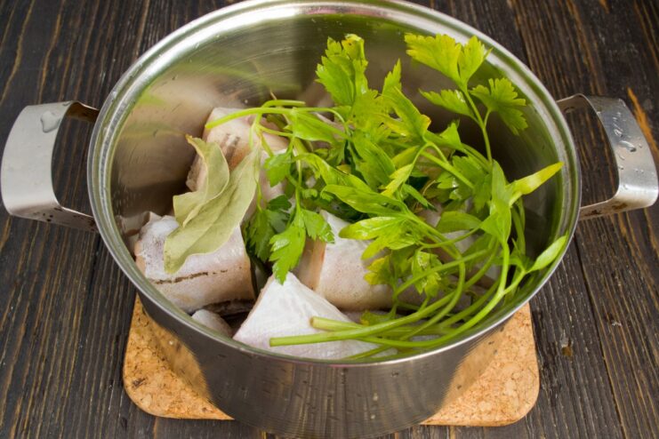 Preparing the Pollock for Boiling with Aromatics Pollock portions, parsley, and bay leaves in a pot, being covered with water before boiling.