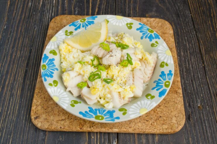 The Final Touch: Serving Pollock with Polish Sauce and Garnish Boiled pollock on a plate, generously topped with Polish sauce and sprinkled with fresh green onions.