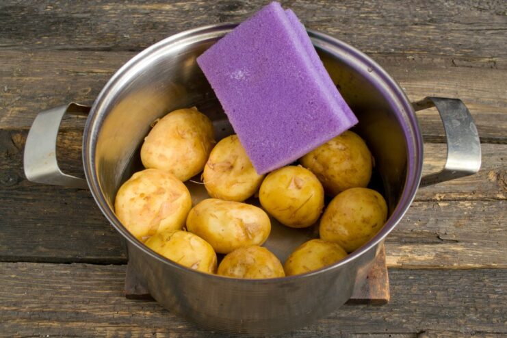 How to Clean New Potatoes Without Peeling Them A person scrubbing new potatoes in a pot of water using a sponge.