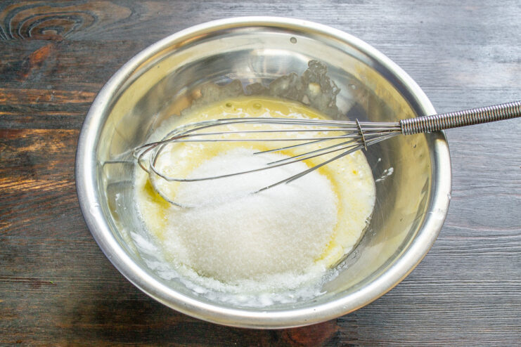 Step 2: Adding Sugar to the Wet Ingredients Adding fine white sugar to the egg and smetana mixture in a bowl.
