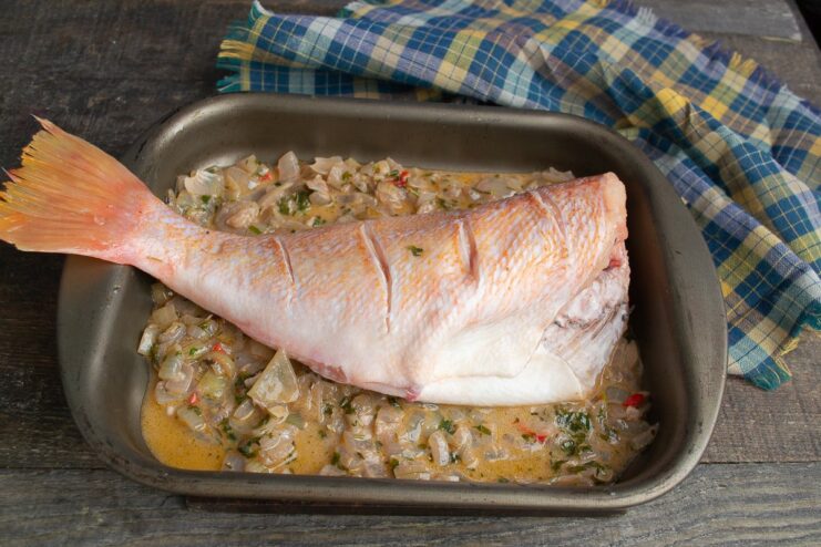 A whole sea bass placed in a baking dish over a creamy sauce, with lemon juice being squeezed on top.