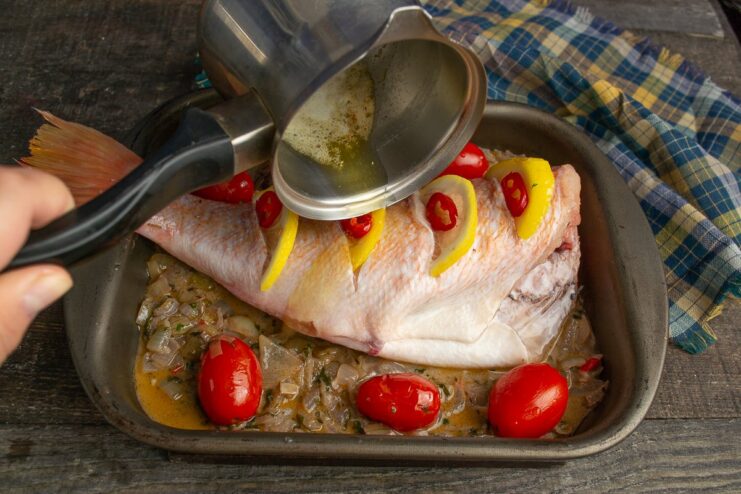 Drizzling melted butter over the sea bass and tomatoes before baking.