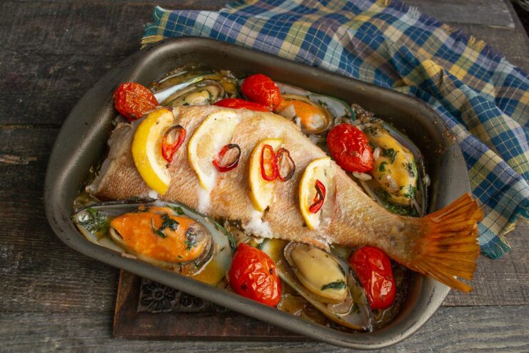 Adding fresh mussels to the baking dish with the sea bass to finish cooking in the oven.