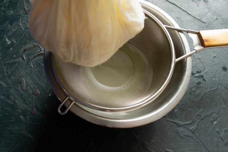 Tying the Cheesecloth — Secure the cheesecloth tightly to form a bundle for draining. A bundle of cheesecloth containing cheese curds, tied securely at the top.