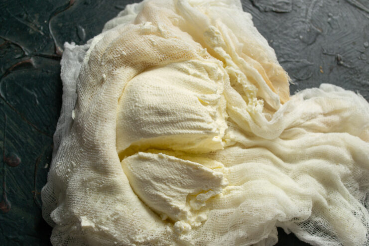 Unwrapping the Finished Cheese — Gently unwrap the cheese, which should be soft and hold its shape. Unwrapping a block of freshly made soft cheese from a piece of cheesecloth.