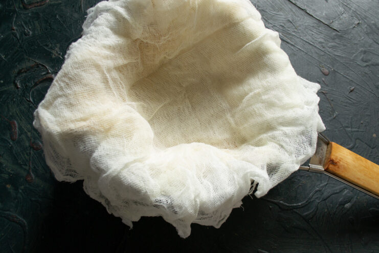 Lining a Colander with Cheesecloth — Use multiple layers to prevent the curds from escaping. A colander lined with multiple layers of white cheesecloth, ready for straining.