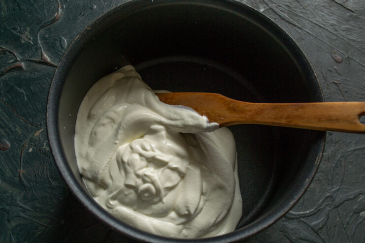 Adding Smetana to the Saucepan — Use a heavy-bottomed saucepan to ensure even heating. A metal saucepan with a portion of white smetana (sour cream) inside.