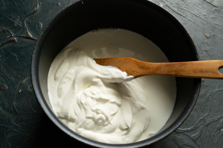 Adding Milk and Salt — Gently mix the ingredients until you have a smooth, uniform mixture. Milk being poured into a saucepan containing smetana, with a pinch of salt added.