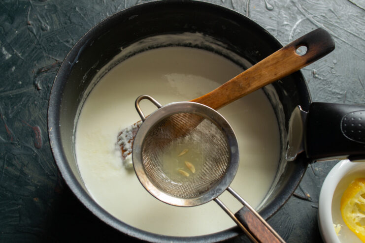 Mixing in the Lemon Juice — Let the mixture rest off the heat to allow the curds to form. Stirring lemon juice into the hot smetana and milk mixture in a saucepan.