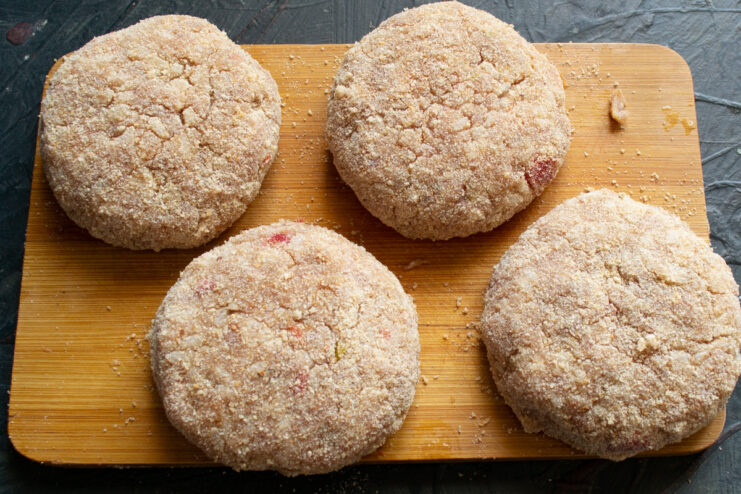 Chilling the Breaded Patties Before Frying Four breadcrumb-coated meat patties on a board, ready for chilling.