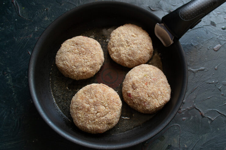 Frying the Patties to a Golden Brown Four meat patties frying in a pan, showing their golden-brown underside.