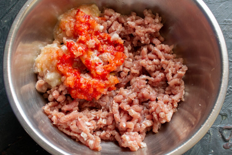 Adding Vegetables to the Meat Grinder Half an onion and half a red bell pepper being put into a meat grinder.