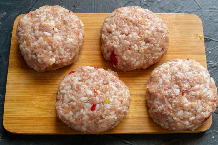 Forming the Raw Meat and Rice Patties Four round, raw meat and rice patties arranged on a cutting board.