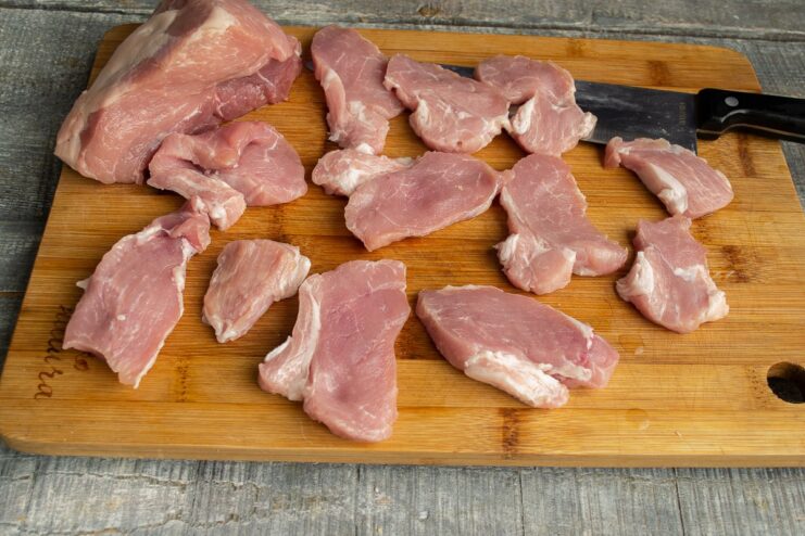 Slicing Pork into Small Pieces for the Stew Raw pork being sliced into small, thin pieces on a cutting board.